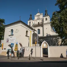 Kościół z wieżami i zegarem, obok tablica "Panie, przymnóż nam wiary". Miejsce pielgrzymek, być może związane z 12 objawieniami maryjnymi uznanymi przez kościół.