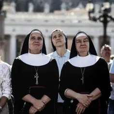 Dwie zakonnice w czarnych habitach z białymi kołnierzami, z krzyżami na szyjach, stoją wśród tłumu.