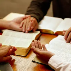 Ludzie trzymają się za ręce nad otwartymi Bibliami, studiując tekst. Może to być streszczenie księgi Hioba, symbolizujące wspólne poszukiwanie odpowiedzi.