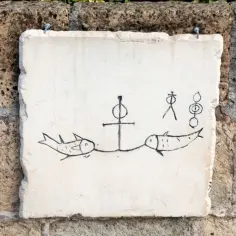Kamienna tablica z rysunkami ryb i symboli, przypominająca inskrypcje z katakumb.