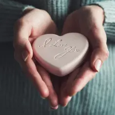 Dłonie trzymają różowe serce z napisem "I Love You". To symbol miłości agape, bezwarunkowej i czystej.