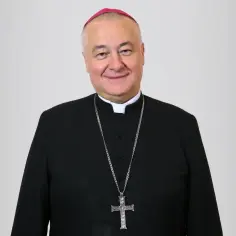 Uśmiechnięty biskup sosnowiecki w czarnej sutannie i z krzyżem na łańcuchu.
