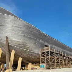 Drewniana konstrukcja przypominająca arkę Noego, wsparta na masywnych belkach, na tle błękitnego nieba.