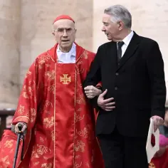 Kardynał w czerwonej szacie wspierany przez mężczyznę w garniturze. Ilu jest kardynałów w Polsce? Trudno ocenić po tym zdjęciu.