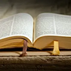 Otwarta księga, być może Stary Testament, z zaznaczonymi fragmentami. Widać tekst, grube, pożółkłe strony i dwie wstążki.