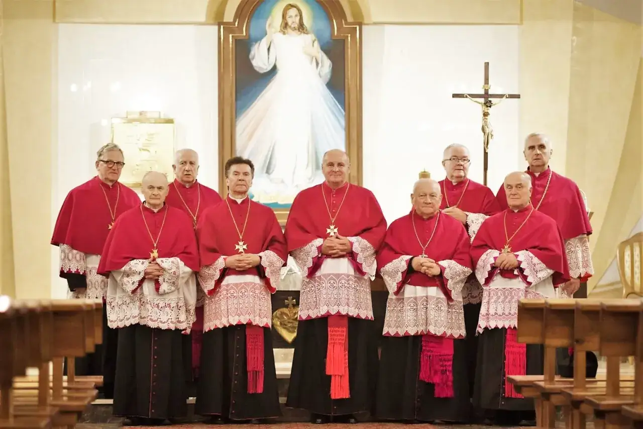 Grupa duchownych w strojach liturgicznych, w tym kanonik, kto to jest? Stoją przed obrazem Jezusa Miłosiernego.