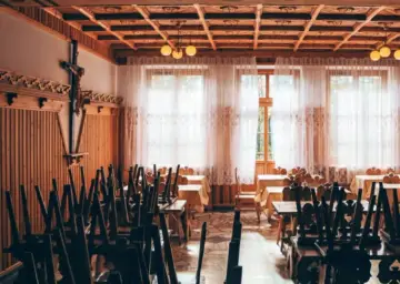 Drewniane wnętrze z krzyżem i stołami nakrytymi obrusami. Widać tu ślady dawnej świetności, być może miejsca związanego z zakonem jezuitów.