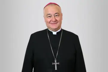 Uśmiechnięty biskup sosnowiecki w czarnej sutannie i z krzyżem na łańcuchu.