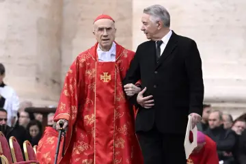 Kardynał w czerwonej szacie wspierany przez mężczyznę w garniturze. Ilu jest kardynałów w Polsce? Trudno ocenić po tym zdjęciu.