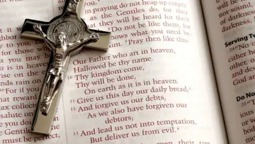Srebrny krzyż na otwartej Biblii, obok fragmentu modlitwy "Ojcze nasz". W tle widać tekst, w tym wersety z psalmów, np. psalm 71.