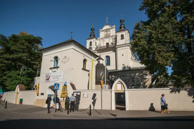 Kościół z wieżami i zegarem, obok tablica "Panie, przymnóż nam wiary". Miejsce pielgrzymek, być może związane z 12 objawieniami maryjnymi uznanymi przez kościół.