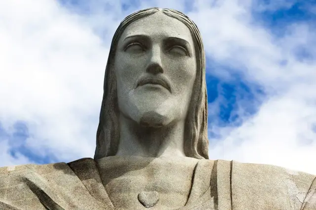 Kamienna twarz Jezusa w Rio, wznosząca się ku błękitnemu niebu z chmurami.