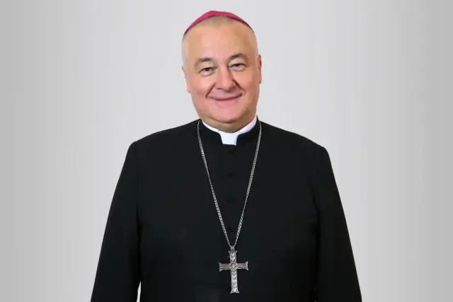 Uśmiechnięty biskup sosnowiecki w czarnej sutannie i z krzyżem na łańcuchu.